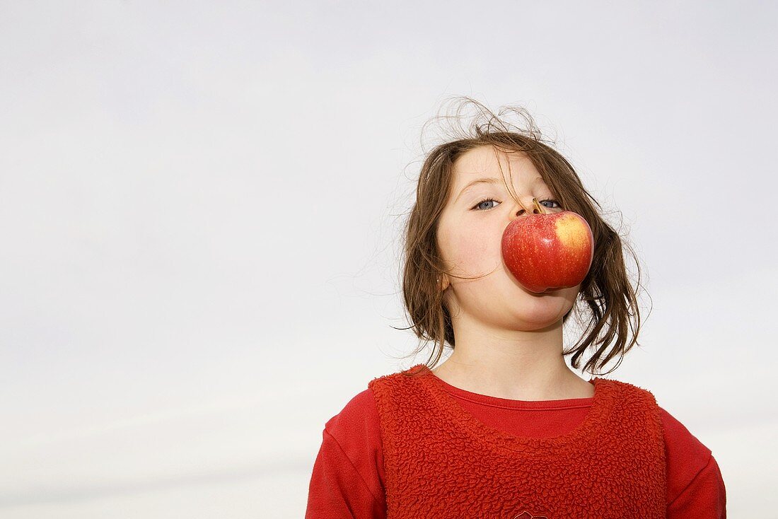 Girl (7-9) with apple in mouth
