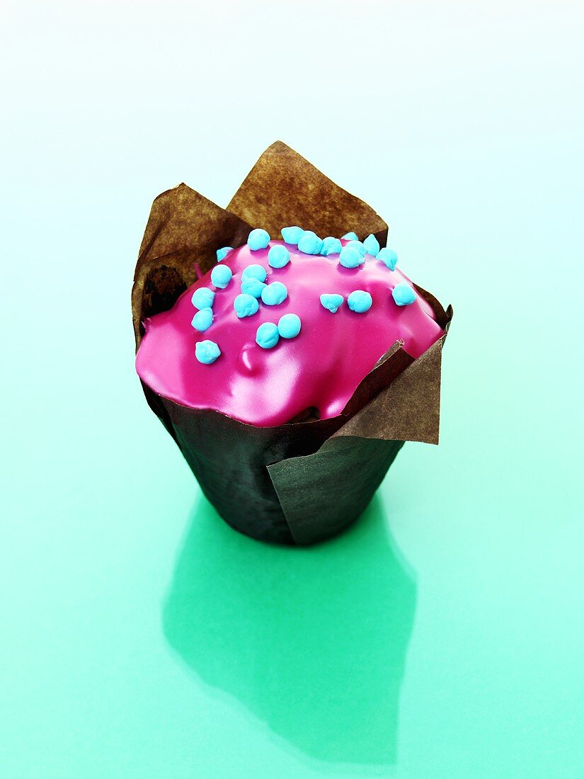 Muffin with pink icing in baking parchment