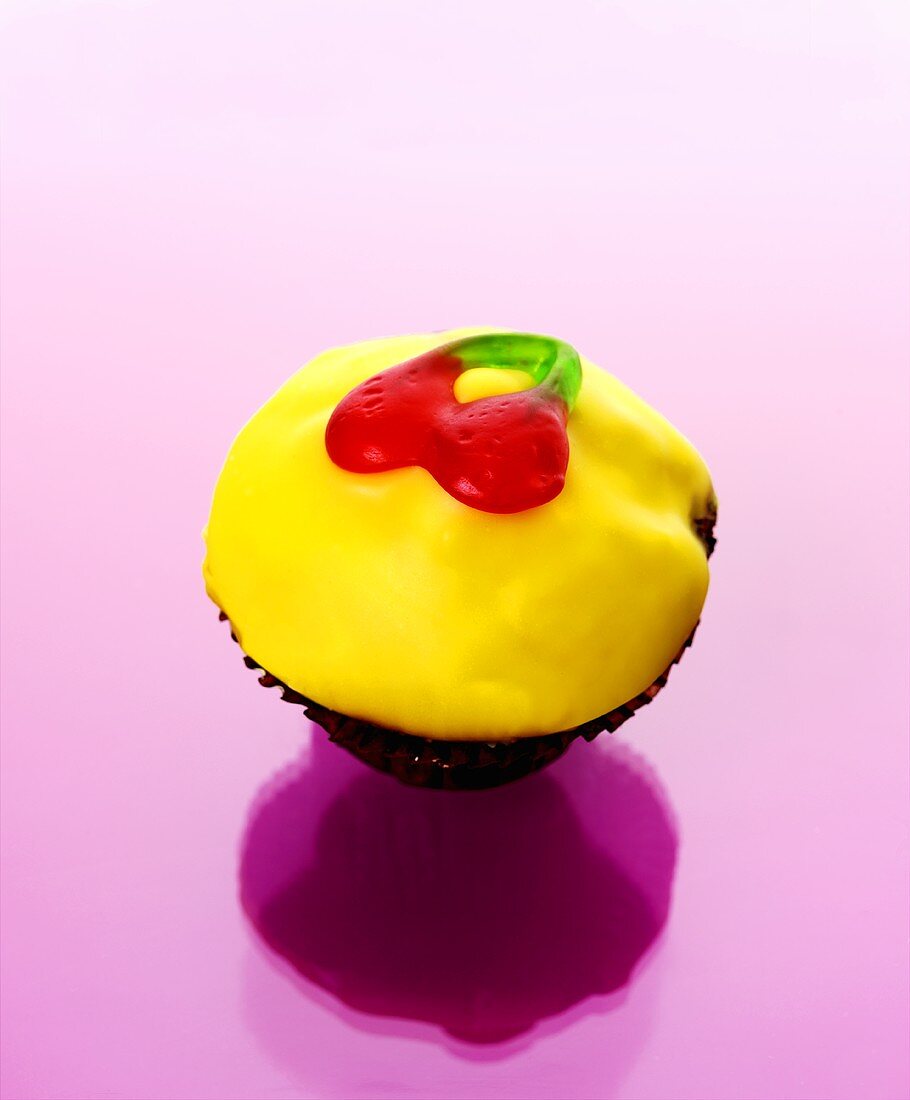 Muffin with yellow icing and jelly cherries