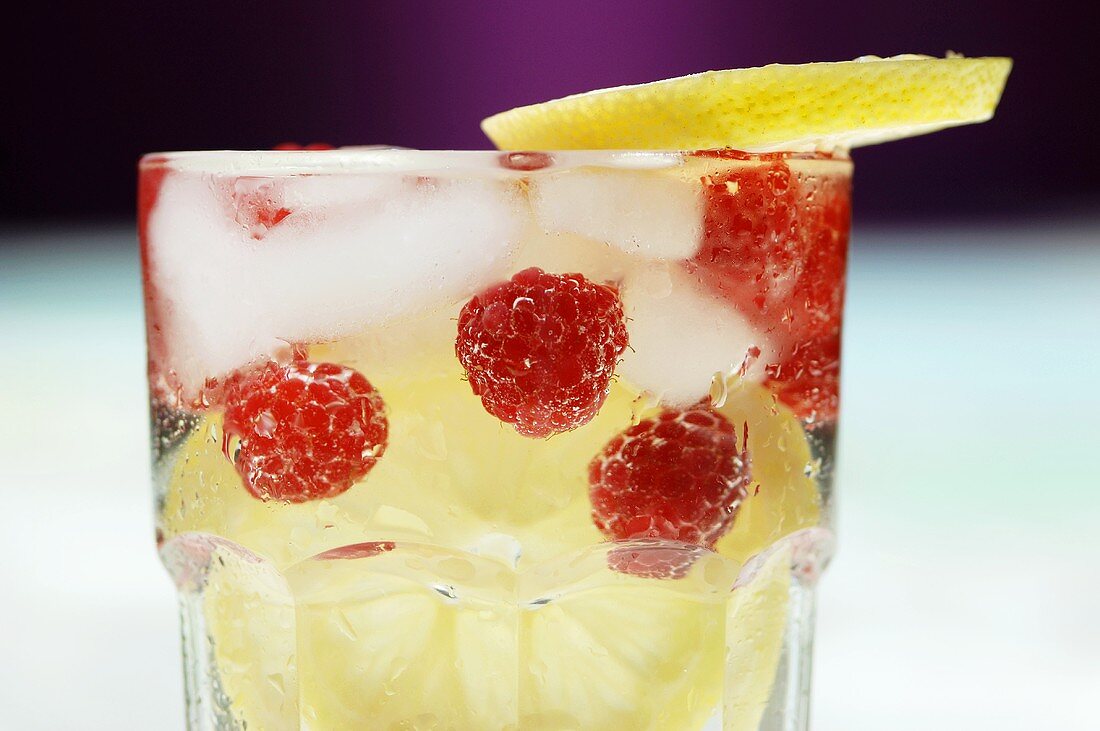 Raspberries, lemon slices and ice cubes in water glass, close-up