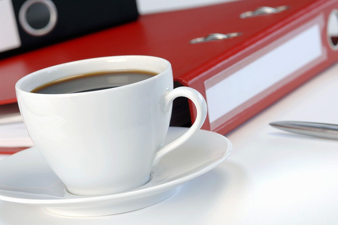 Cup of coffee in front of folders, close-up