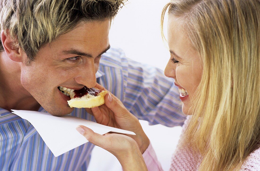 Woman feeding man cake with jam, close-up