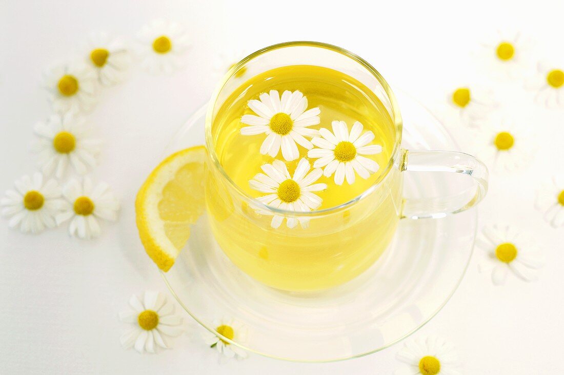 Chamomile tea in cup with flowers and lemon, close-up