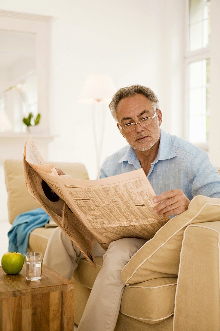 Älterer Mann liest die Zeitung auf dem Sofa