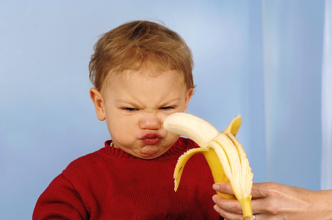 Woman offering banana to reluctant child