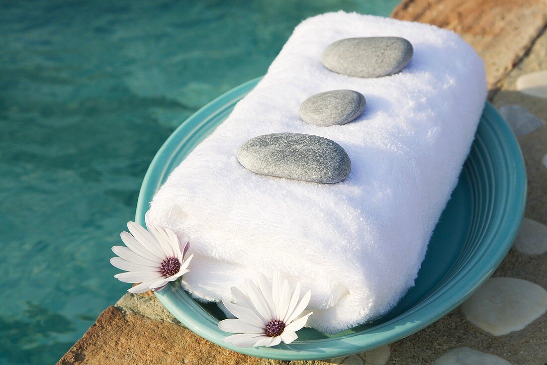 Handtuch, Steine und Blumen auf Teller am Swimmingpool