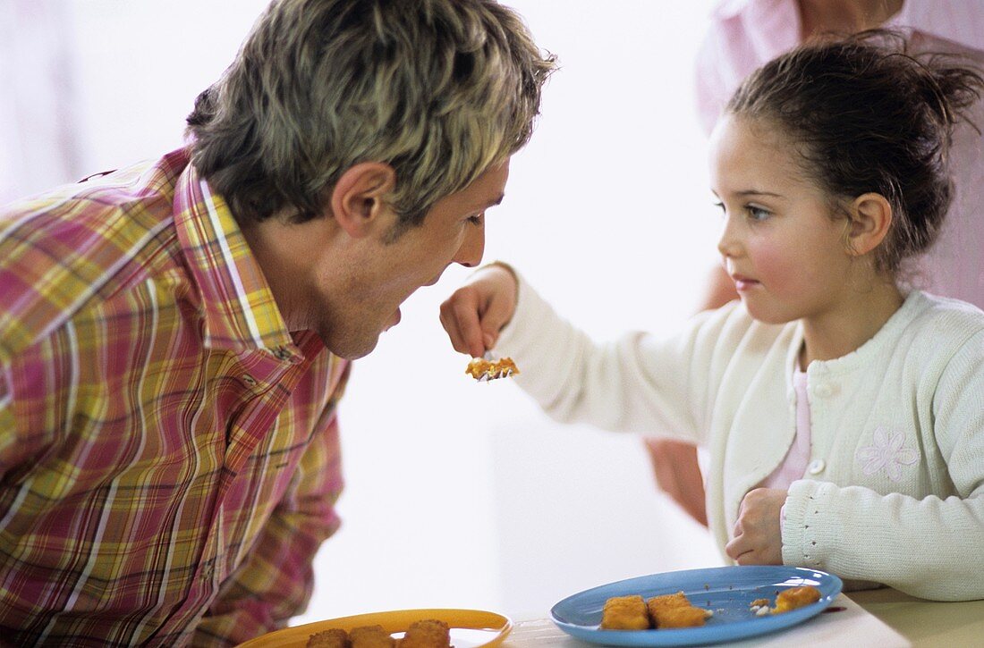 Kleines Mädchen füttert Vater mit Fischstäbchen