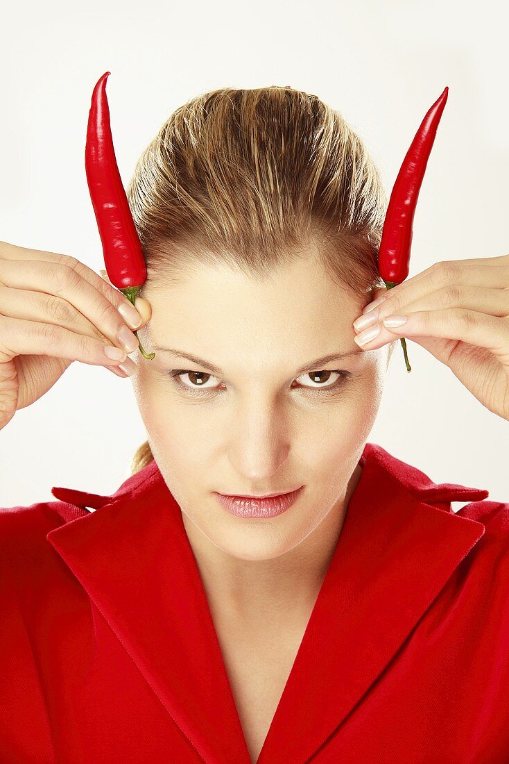Young woman holding chili on head, simulating horns, portrait