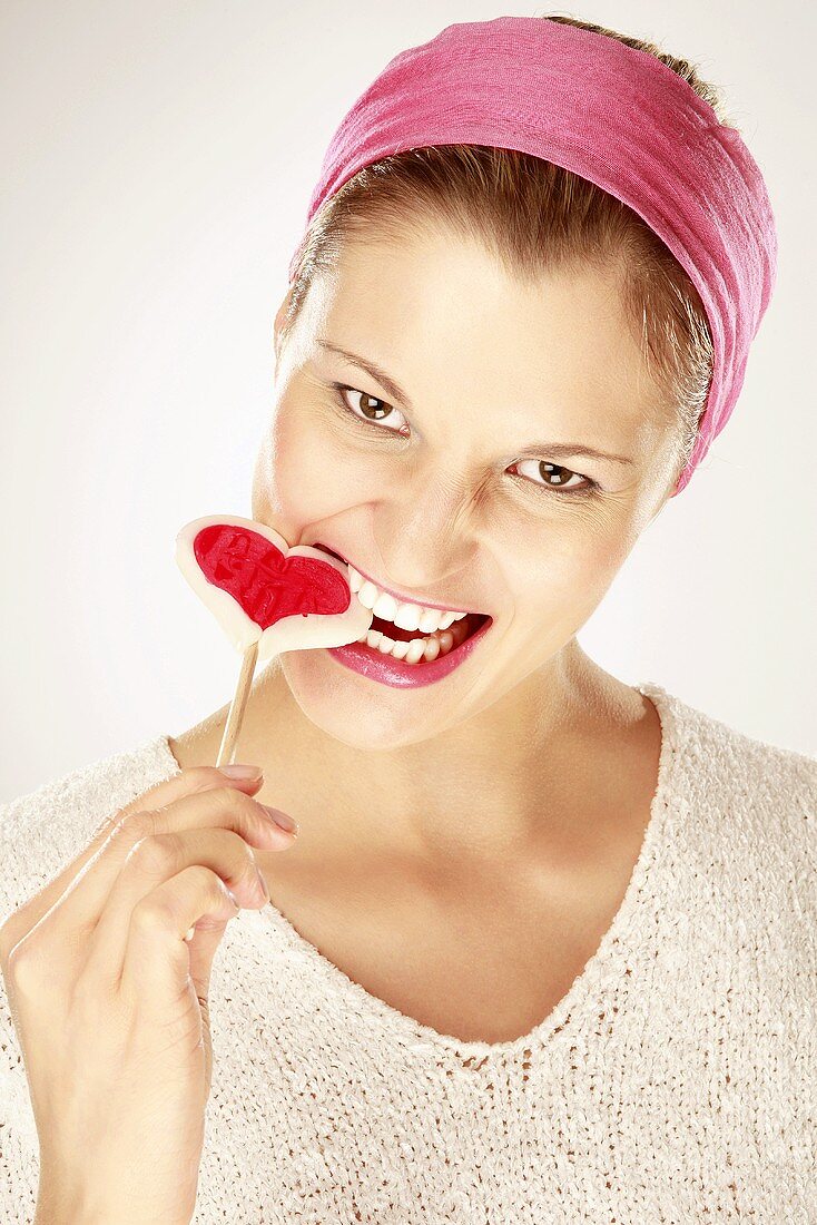 Young woman eating heart shaped lollipop, close-up, portrait