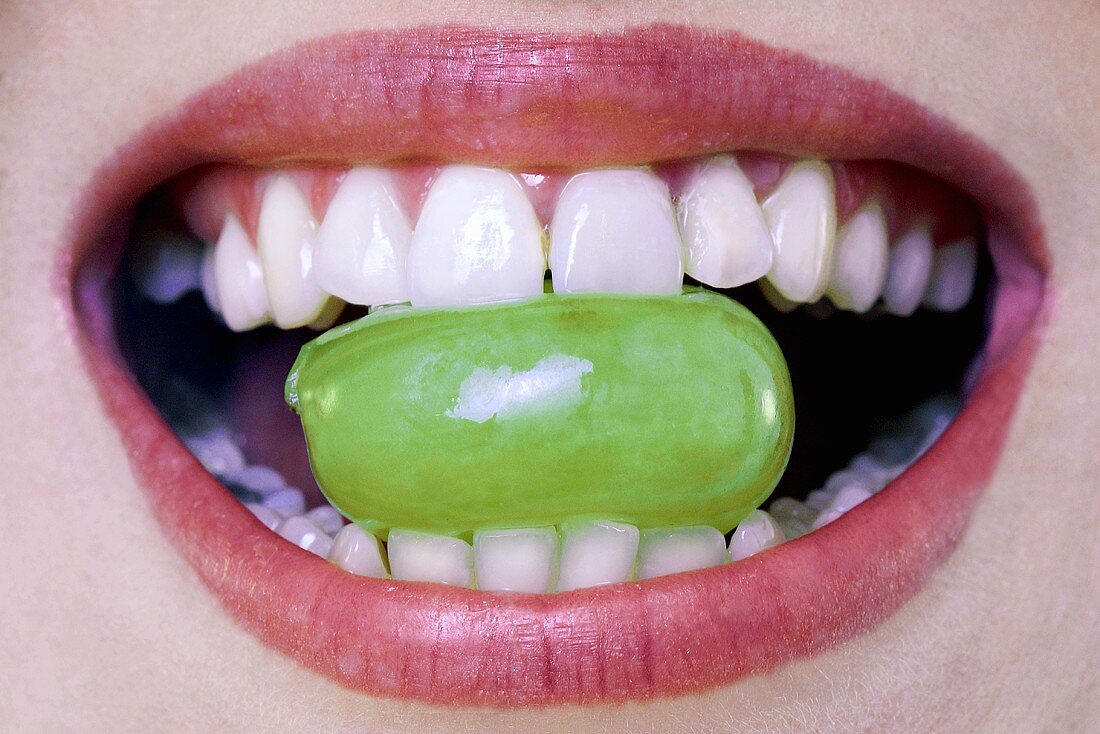 Woman holding grape between teeth, close-up