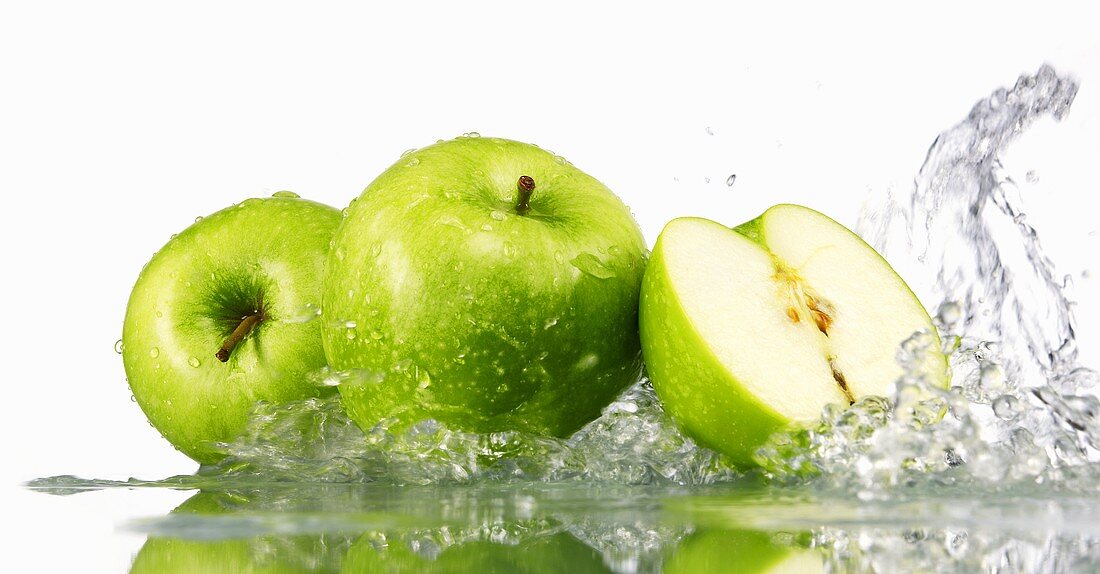 Grüne Äpfel, ganz und halbiert, von Wasser umspült