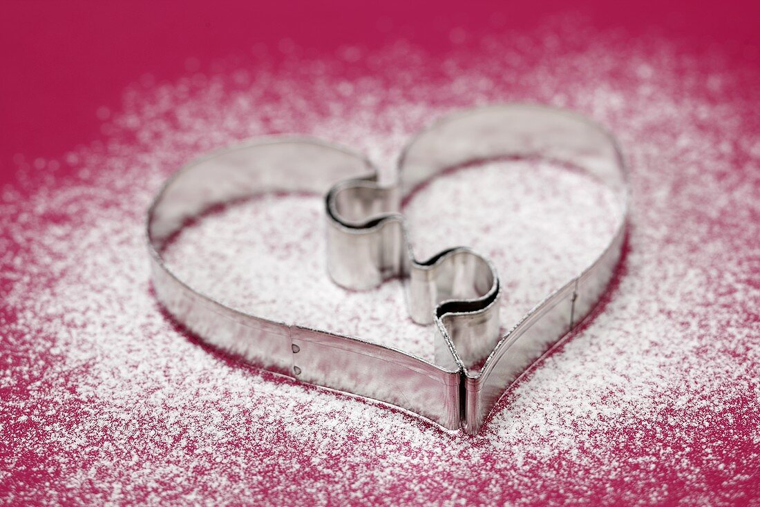 Heart-shaped biscuit cutter on icing sugar