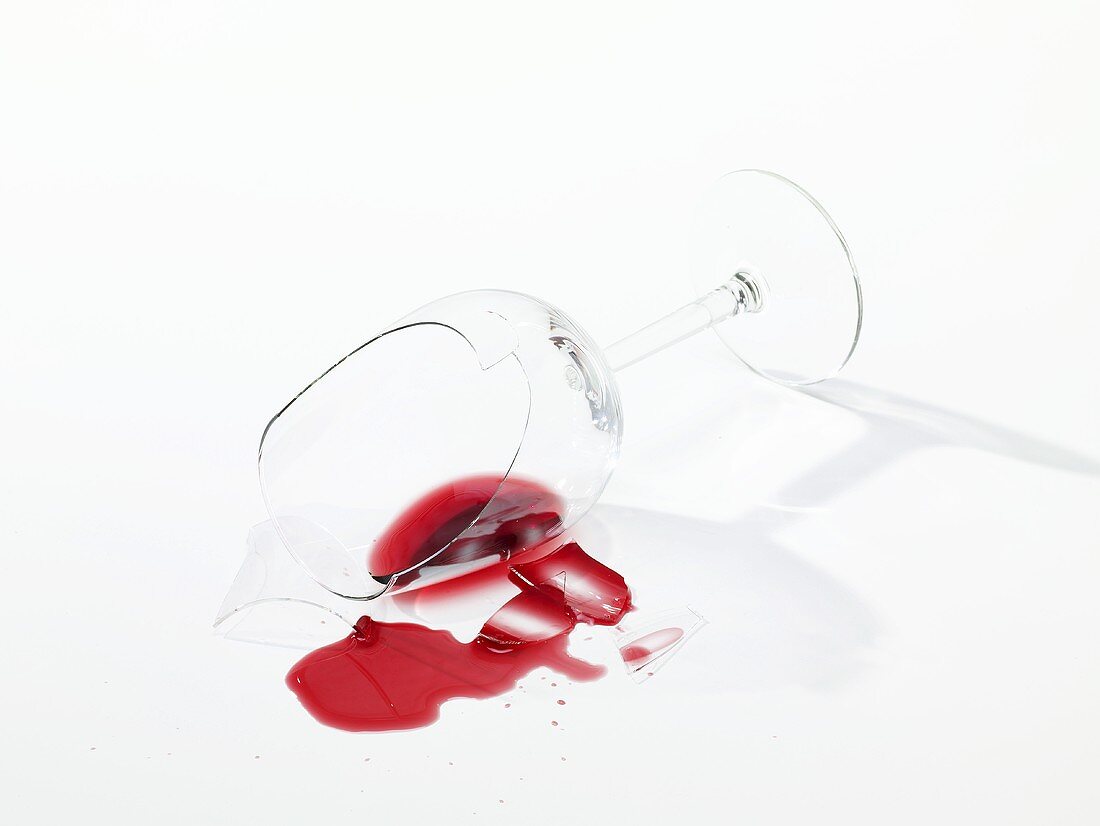 Zerbrochenes Weinglas mit verschüttetem Rotwein