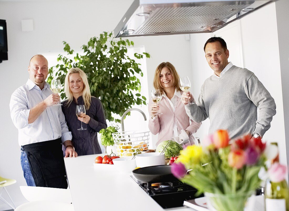 Two couples raising glasses of wine in kitchen