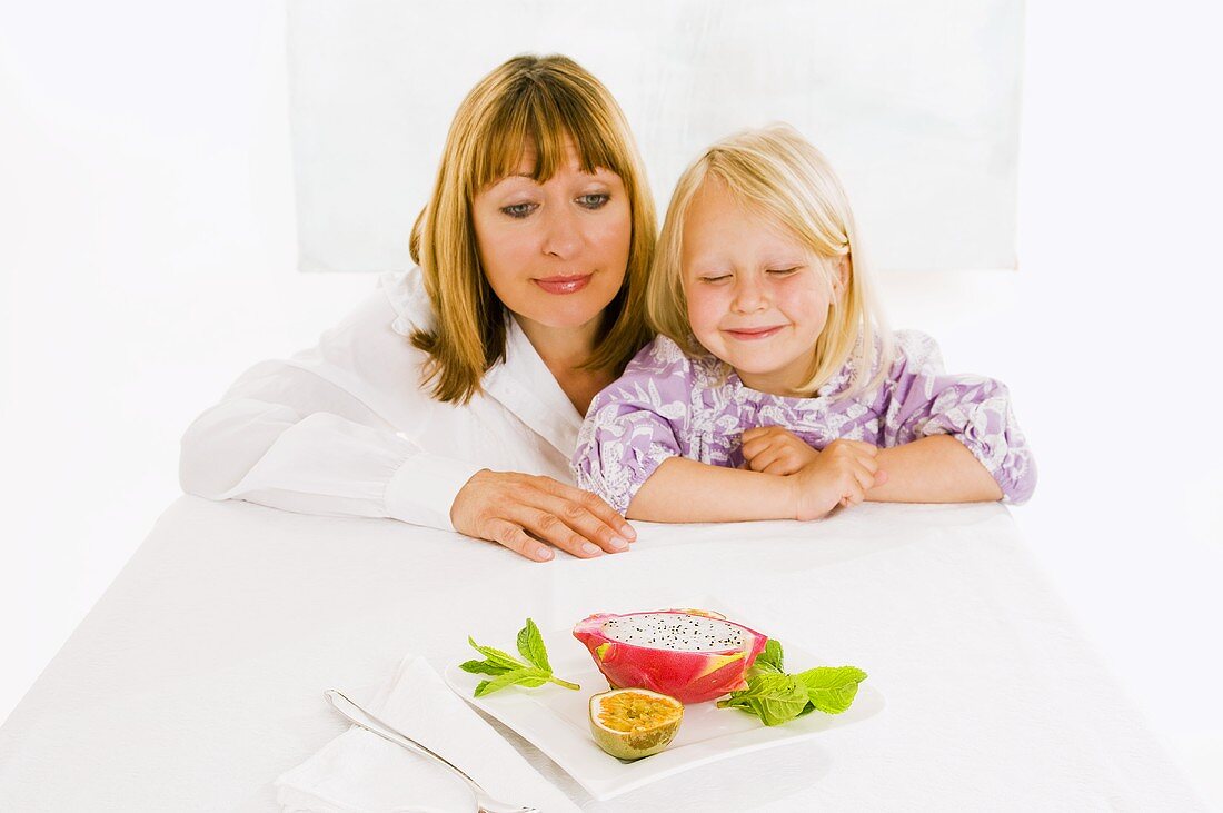 Mother and daughter sitting at table with plate of fruit