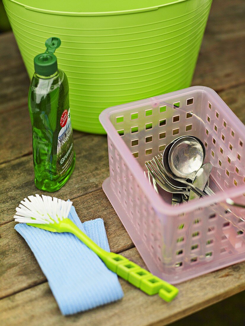 Besteck, Spülmittel, Bürste und Plastikwanne auf Holztisch