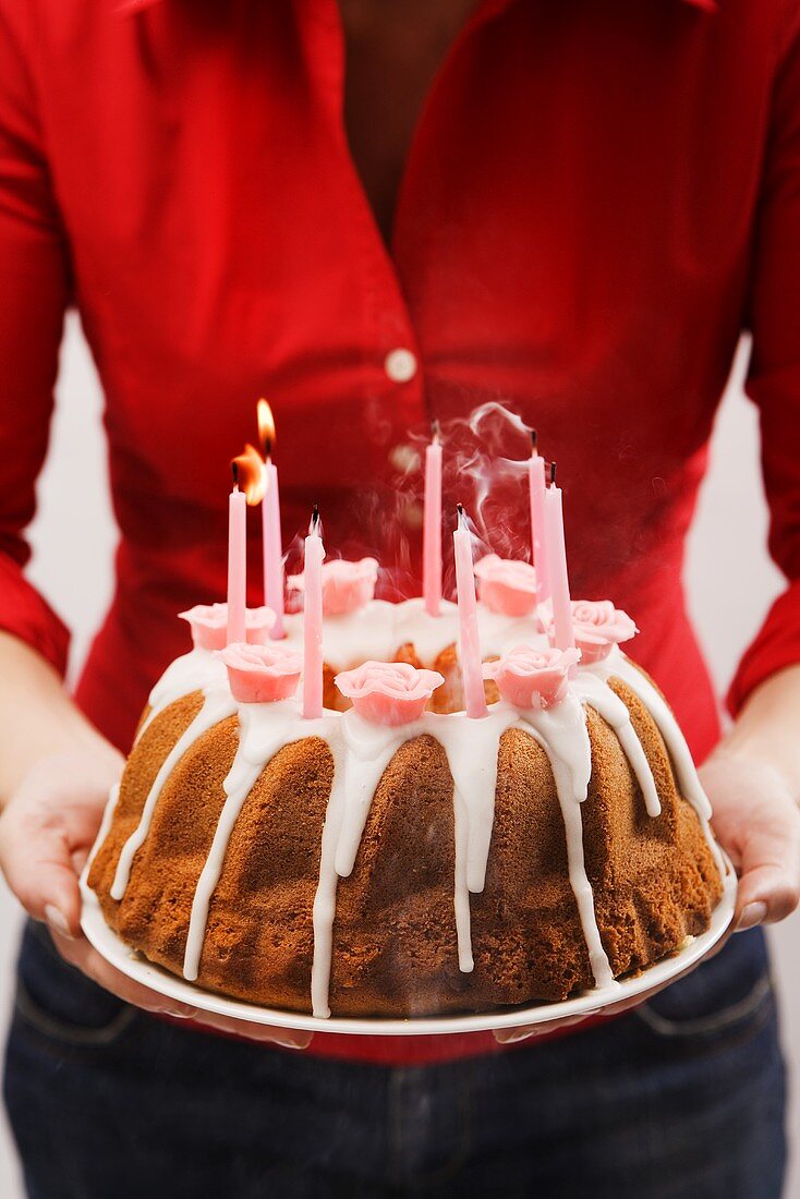 Frau hält Geburtstagsnapfkuchen mit Zuckerguss und Kerzen