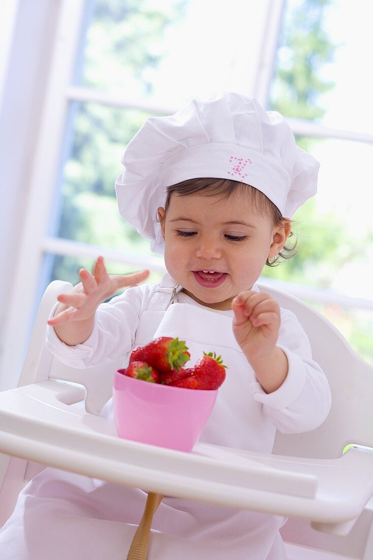 Little girl in chef's hat eating strawberries