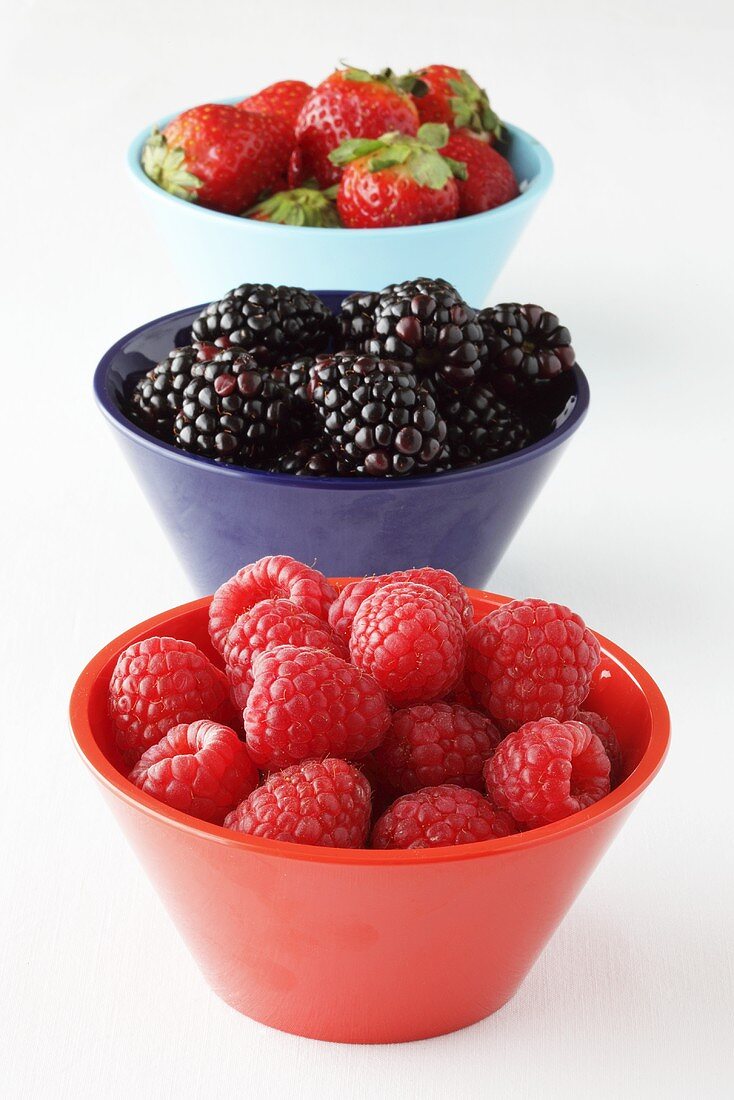 Three bowls containing strawberries, blackberries and raspberries