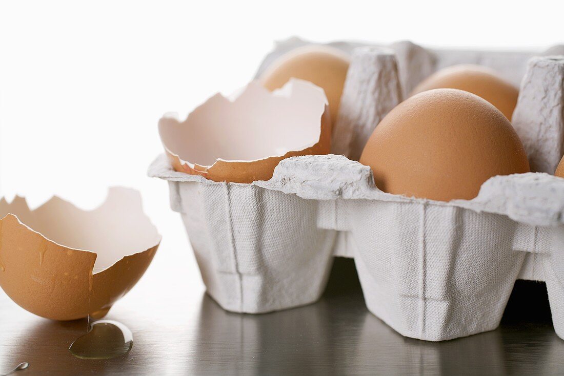 Eier im Eierkarton, eines davon aufgeschlagen