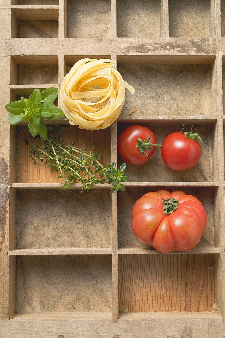 Bandnudeln, Tomaten und frische Kräuter im Setzkasten