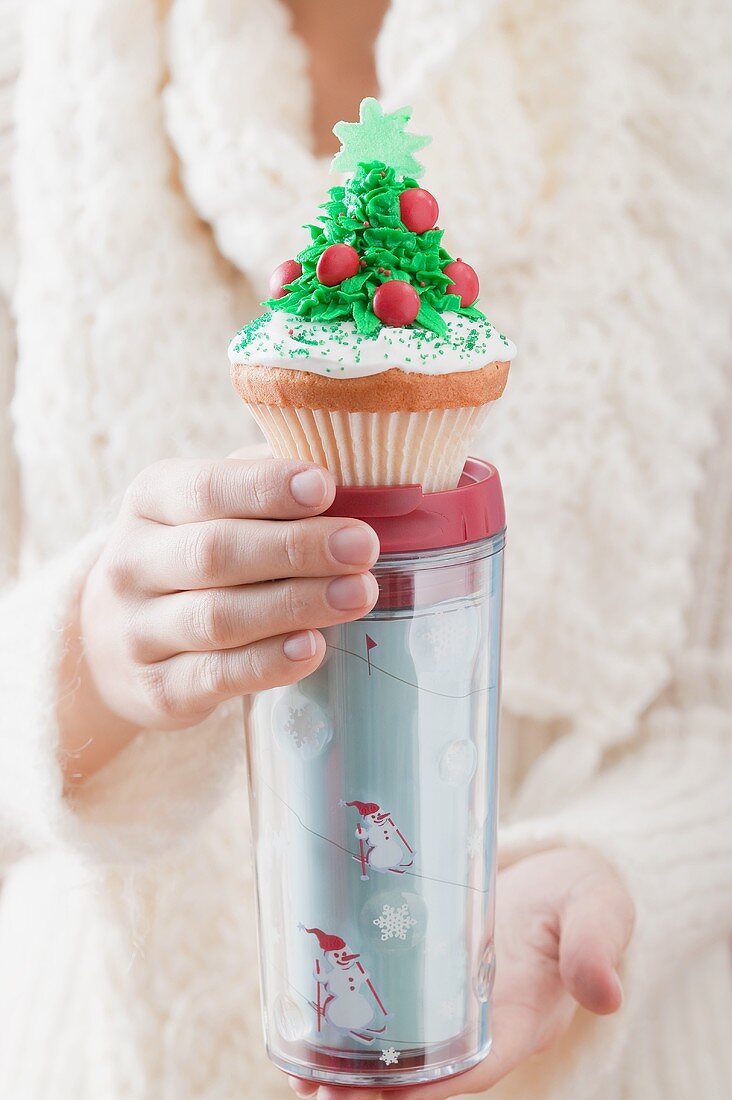 Frau hält Cupcake auf Thermobecher zu Weihnachten