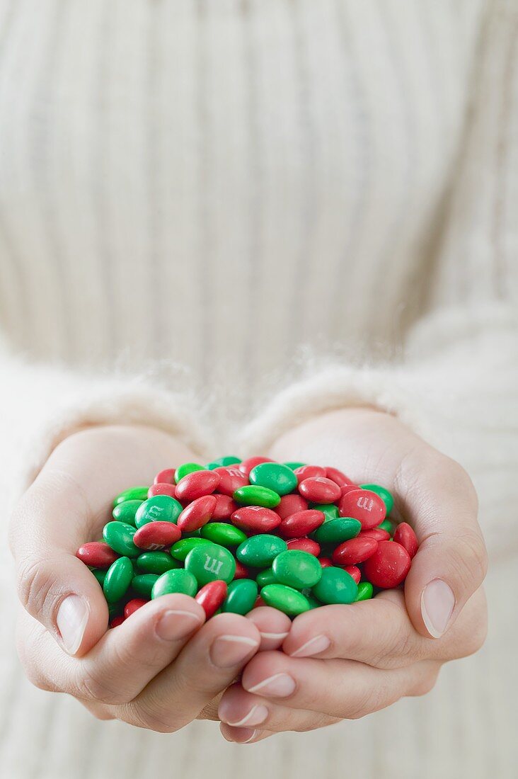 Hands holding red and green chocolate beans (Christmas)
