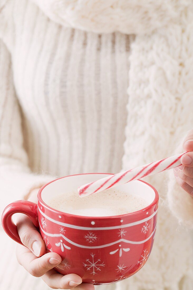 Frau hält Tasse Kakao und Zuckerstange (weihnachtlich)