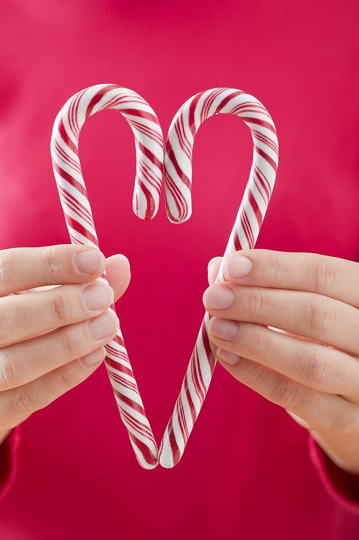 Woman holding two candy canes together to form a heart