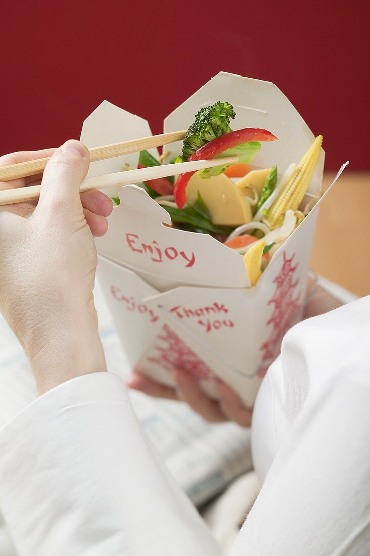 Woman eating Asian vegetable dish out of take-away container