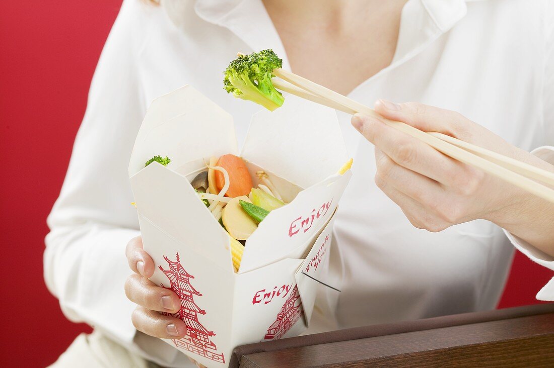 Frau isst asiatisches Gemüsegericht im Take-Out-Behälter
