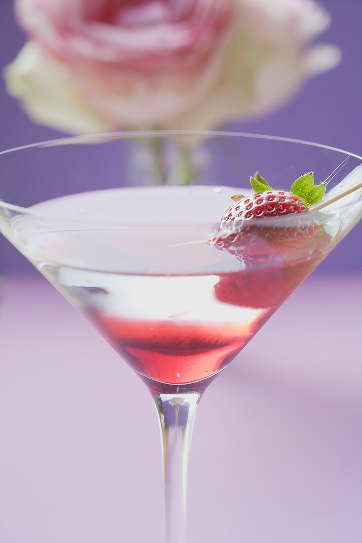 Martini mit Erdbeere im Glas, Rose im Hintergrund