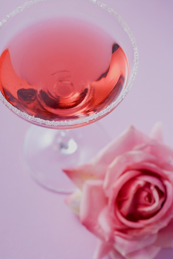 Rosenlikör im Glas mit Zuckerrand, daneben Rosenblüte