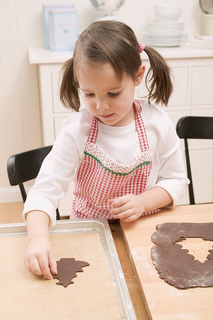 Kleines Mädchen legt Schokoladenplätzchen auf Backblech