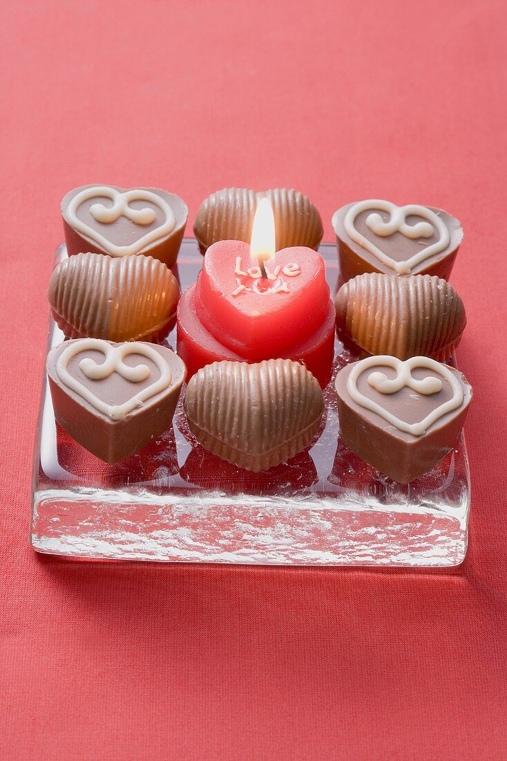 Herzförmige Kerze, umgeben von Schokoladenpralinen
