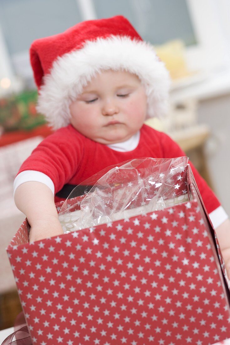 Baby in Father Christmas hat reaching into opened parcel