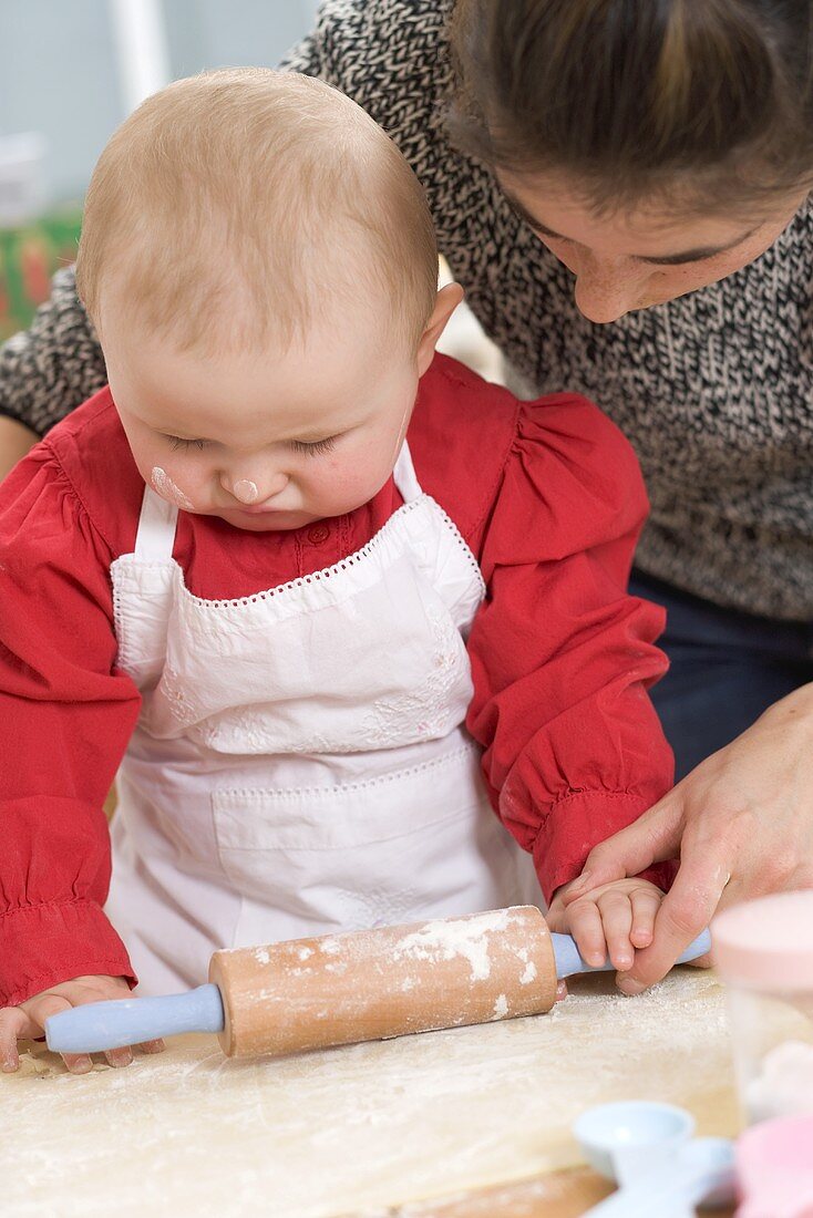 Mother showing baby how to roll out dough