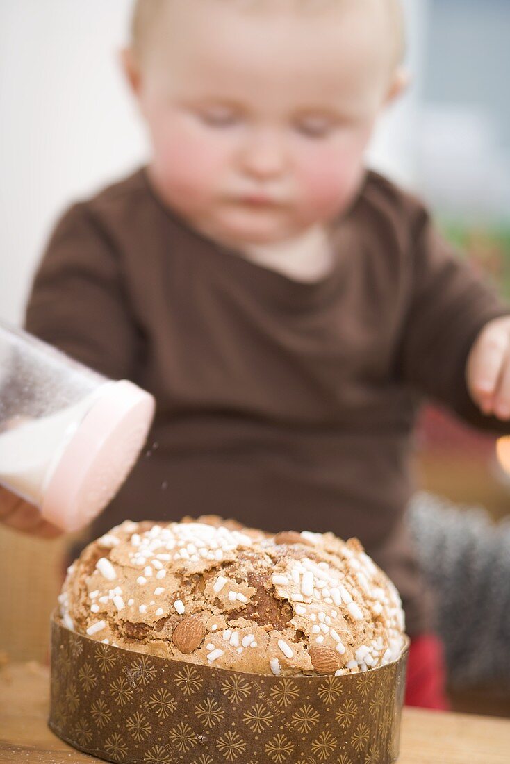 Kleinkind streut Zucker auf Mandelkuchen
