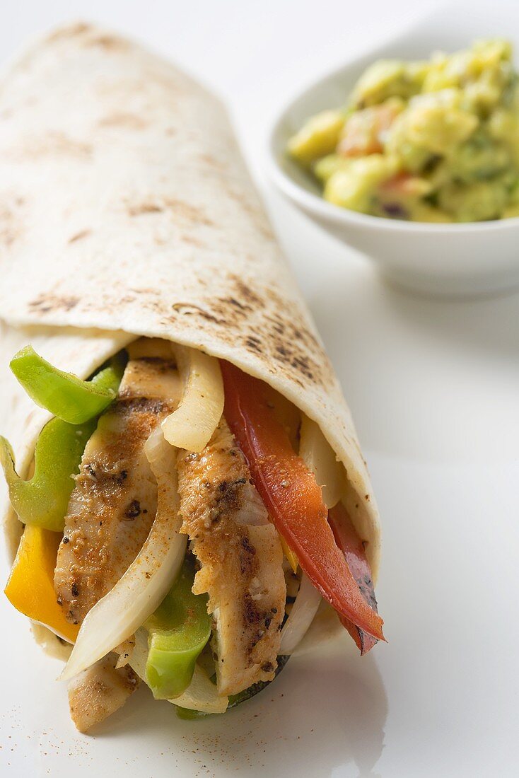 Wrap filled with chicken and peppers, guacamole beside it
