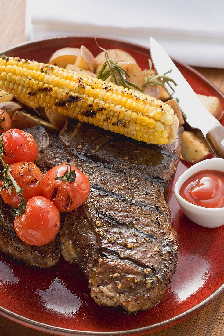 Grilled steak, corn on the cob, cherry tomatoes, potatoes, ketchup