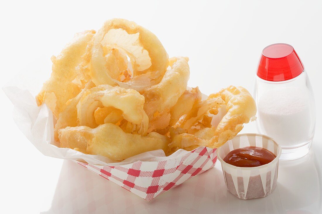 Deep-fried onion rings in cardboard container, ketchup, salt