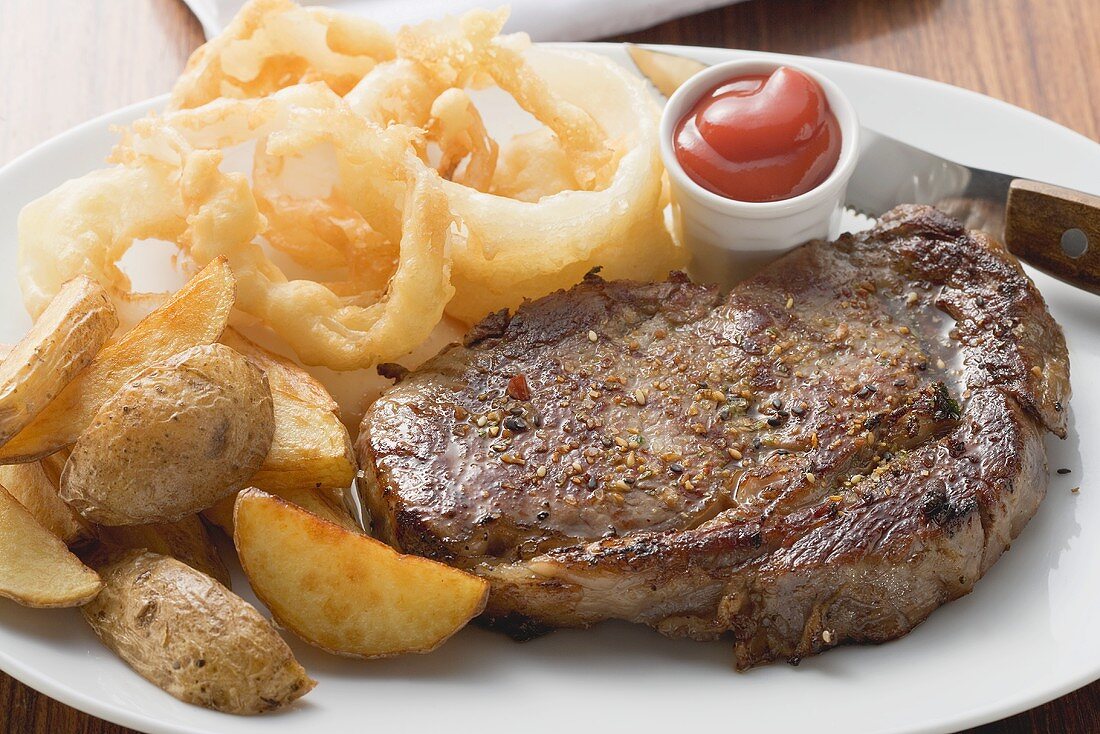 Rib-eye steak with onion rings, ketchup and potato wedges