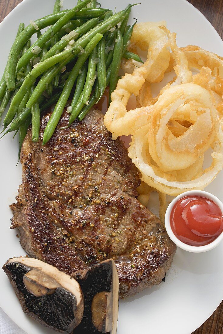 Ribeye Steak mit Bohnen, Zwiebelringen, Ketchup und Pilzen