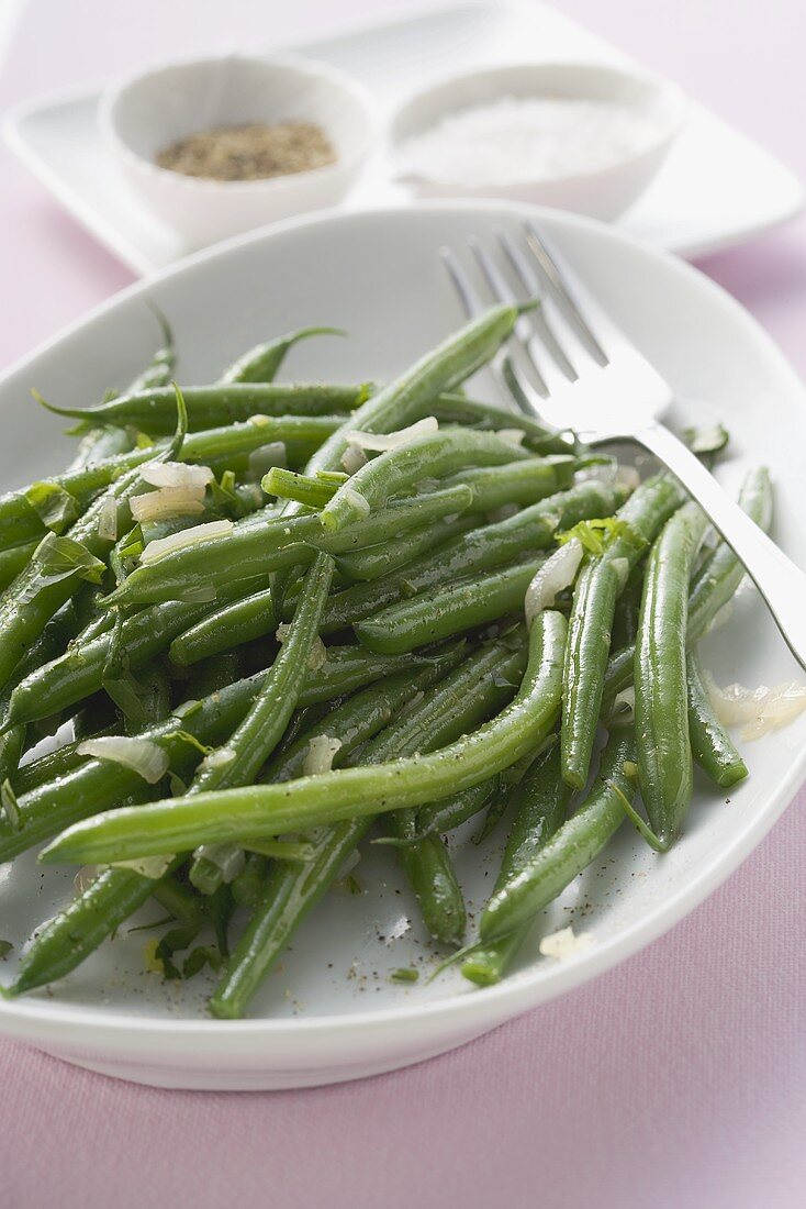 Green beans with onions, salt and pepper in background