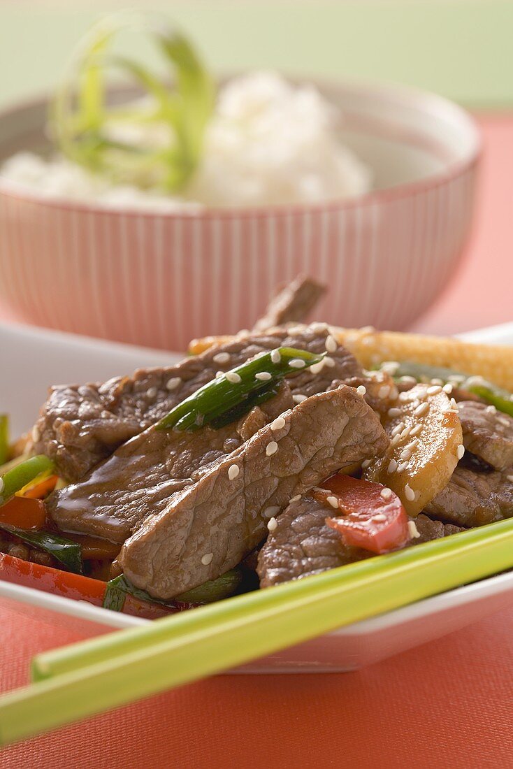 Beef with vegetables & sesame seeds, rice in background (Asia)