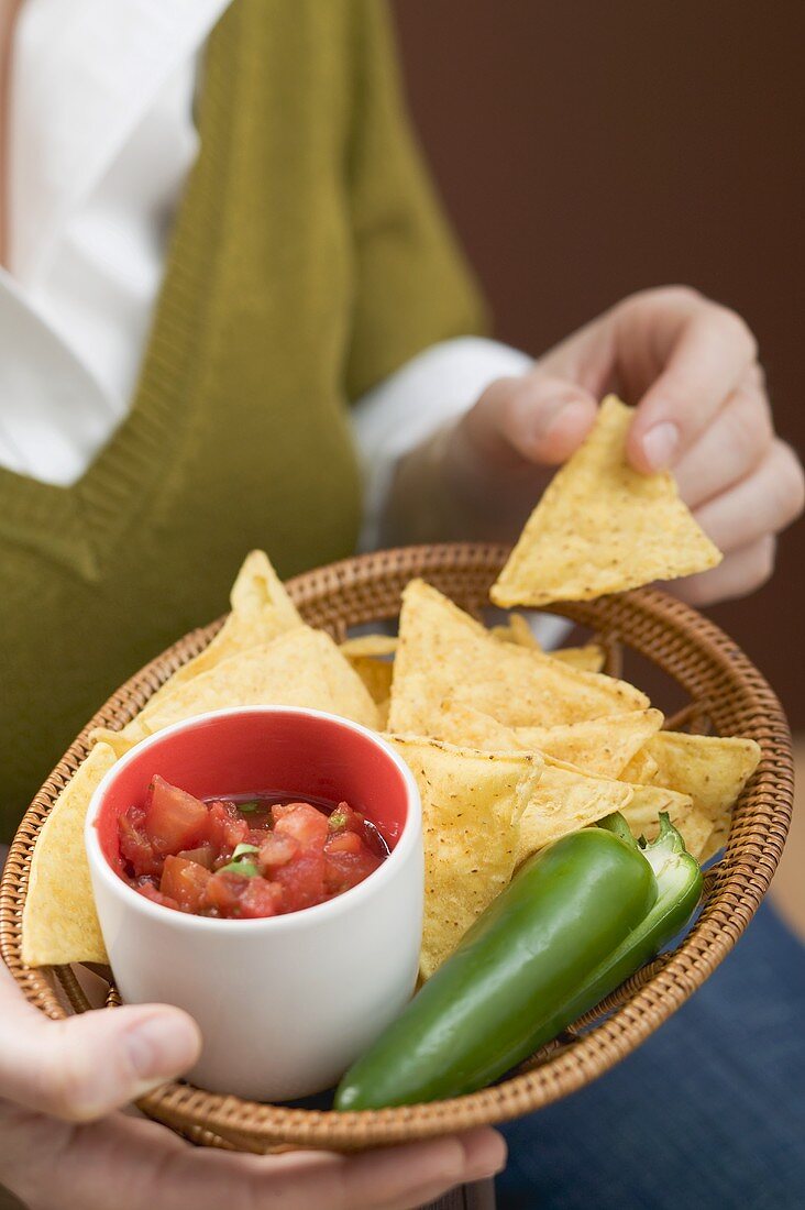 Woman holding basket of nachos with salsa and chilli