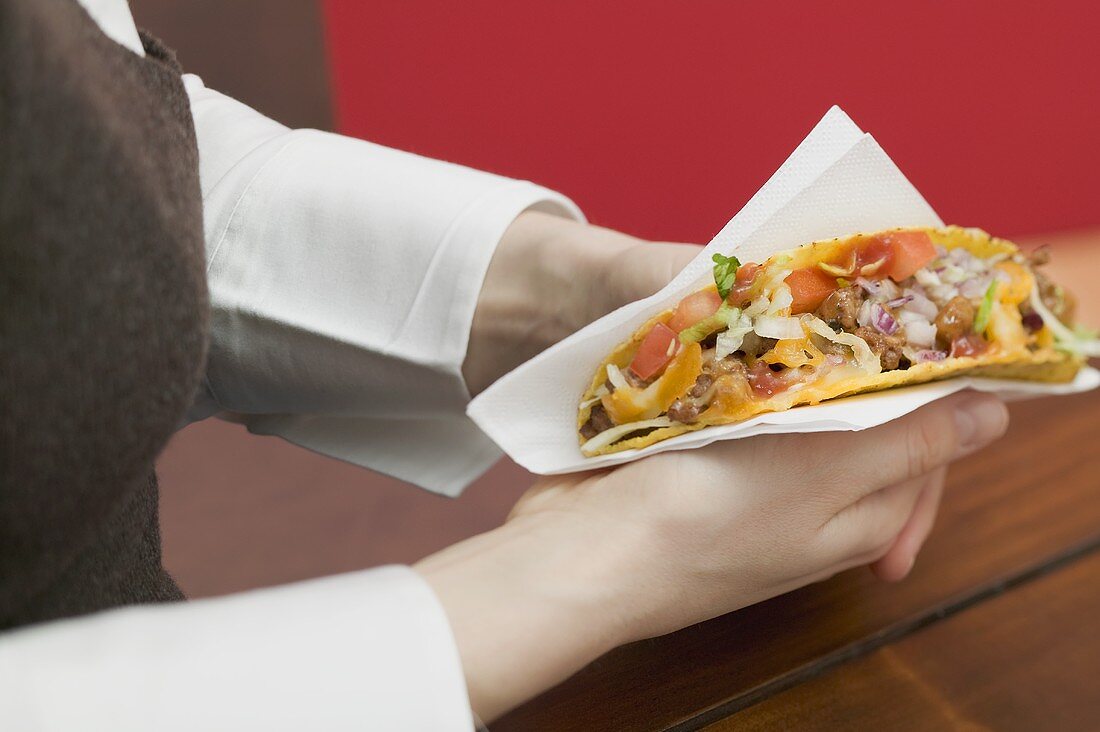 Frau hält Taco mit Hackfleisch in Papierserviette
