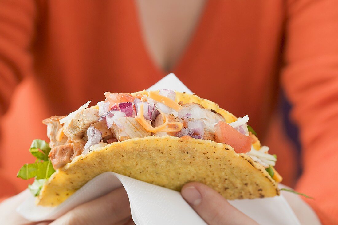 Woman holding chicken taco on paper napkin