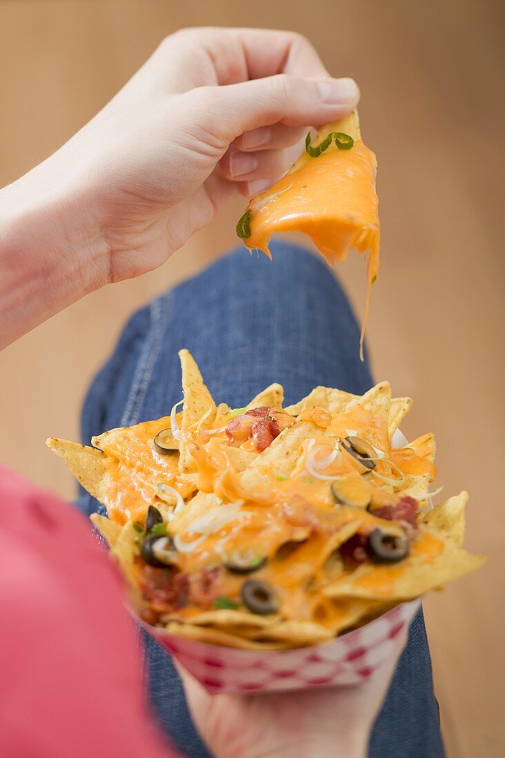 Frau hält überbackene Nachos im Pappschälchen