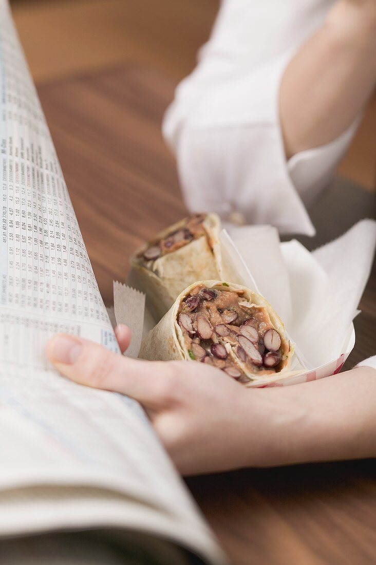 Frau mit Burrito beim Zeitunglesen